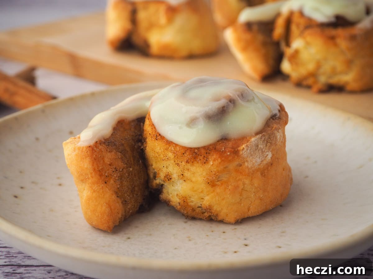 Air Fryer Cinnamon Rolls: Quick, Fluffy Homemade Recipe 2 Air fryer cinnamon roll on a plate, with rolls in background.