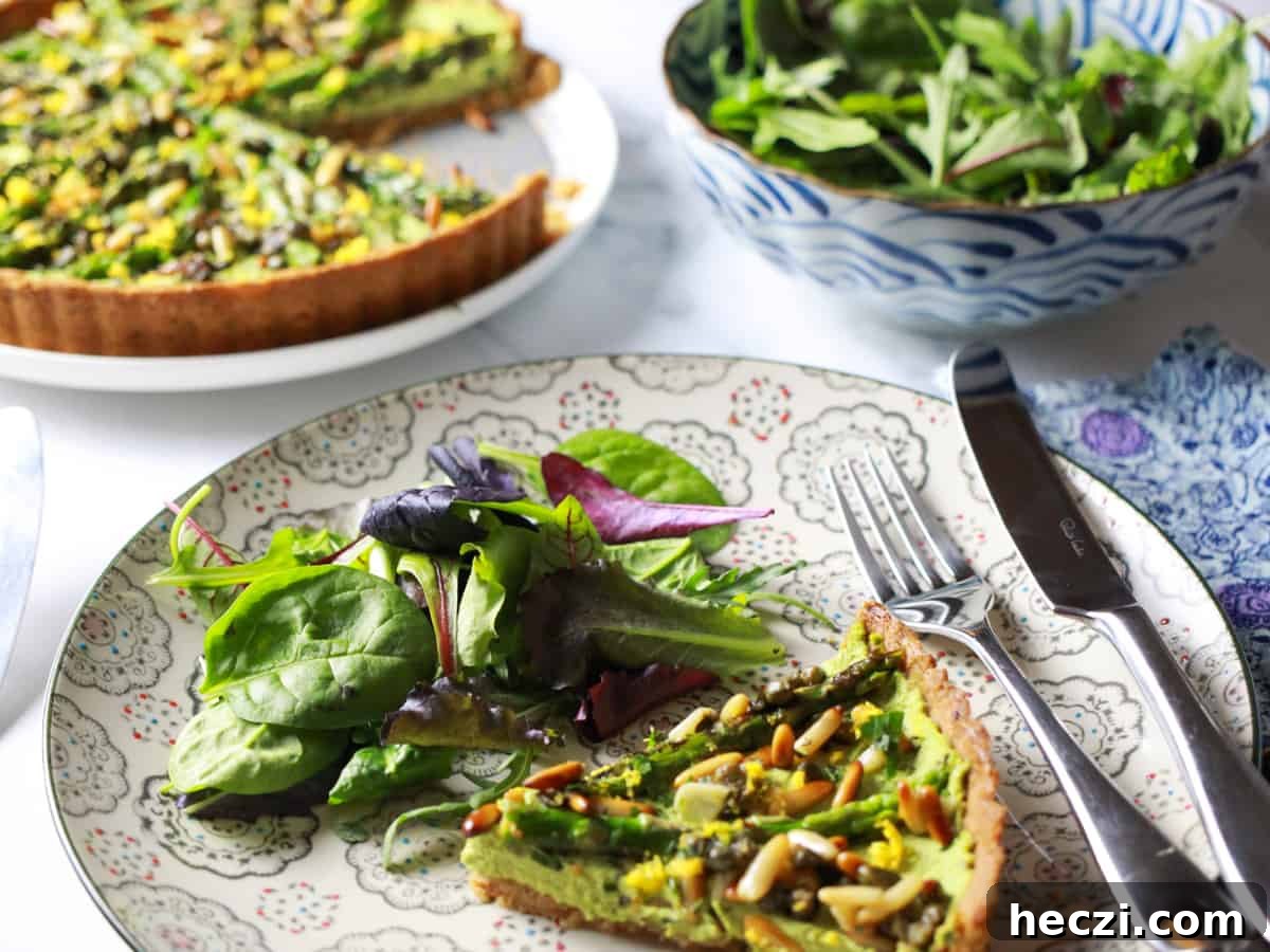 Photo of a plate with a portion of asparagus and pesto macadamia tart and some salad and a fork, with the full tart and a bowl of salad in the background.