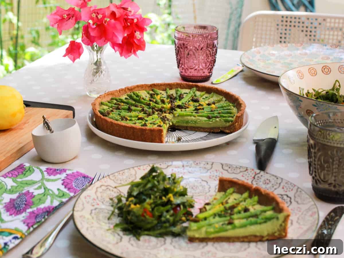 a table set for lunch in the garden with flowers on the table and an asparagus tart in the middle with a portion of tart and salad served on the nearest plate.