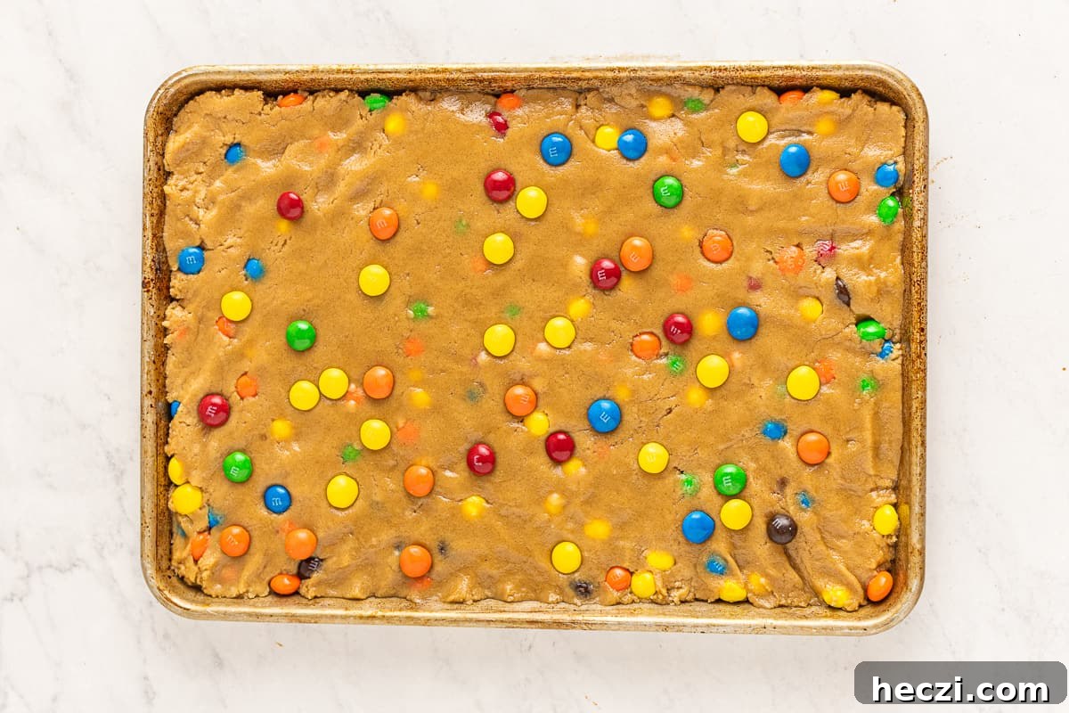 Peanut butter blondie dough spread into a baking sheet, dotted with M&Ms.