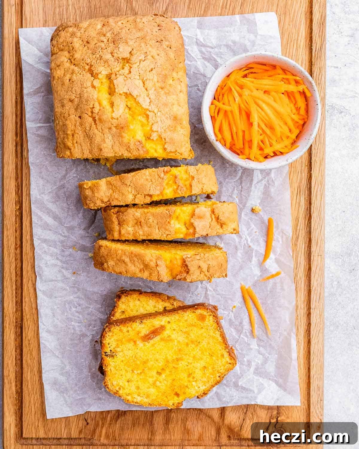 Extra-Moist Carrot Cake Loaf Recipe Packed with Flavor 9 Carrot cake loaf on parchment paper, sliced into thick pieces, with a bowl of shredded carrots nearby.