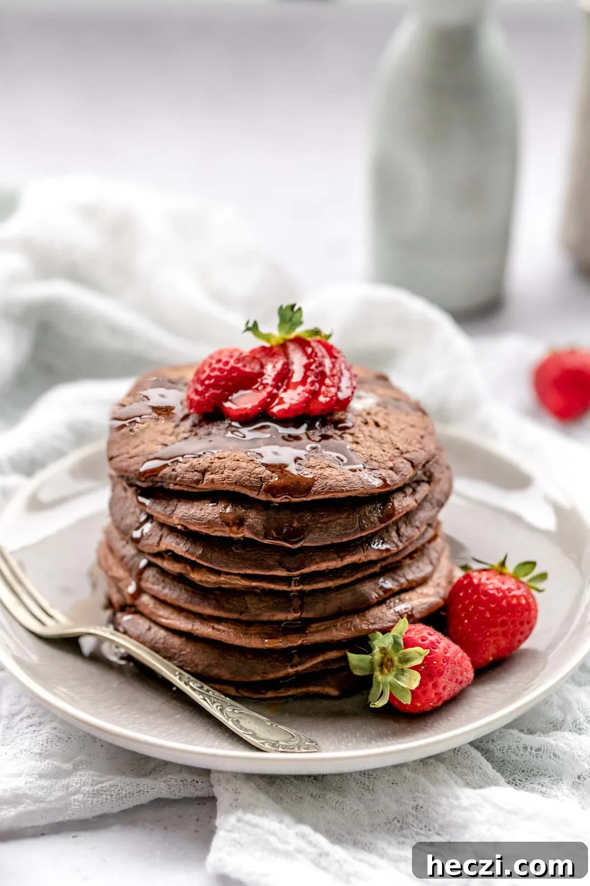 Chocolate pancakes topped with strawberries and dripping with syrup on a plate with a vintage fork.
