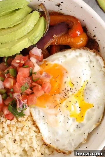 Breakfast burrito bowl topped with avocado and pico de gallo in a speckled bowl.