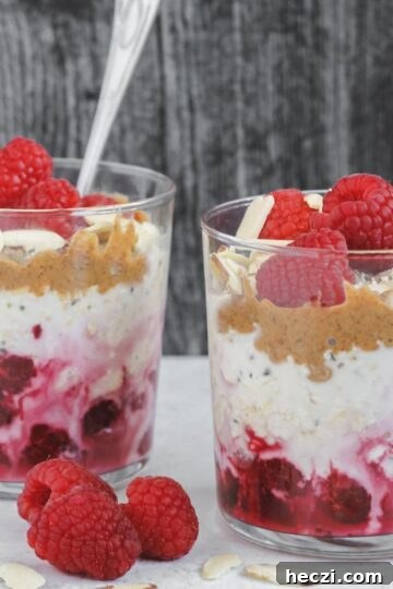 Two glass cups filled with layers of oats, raspberries, almond butter and almonds.