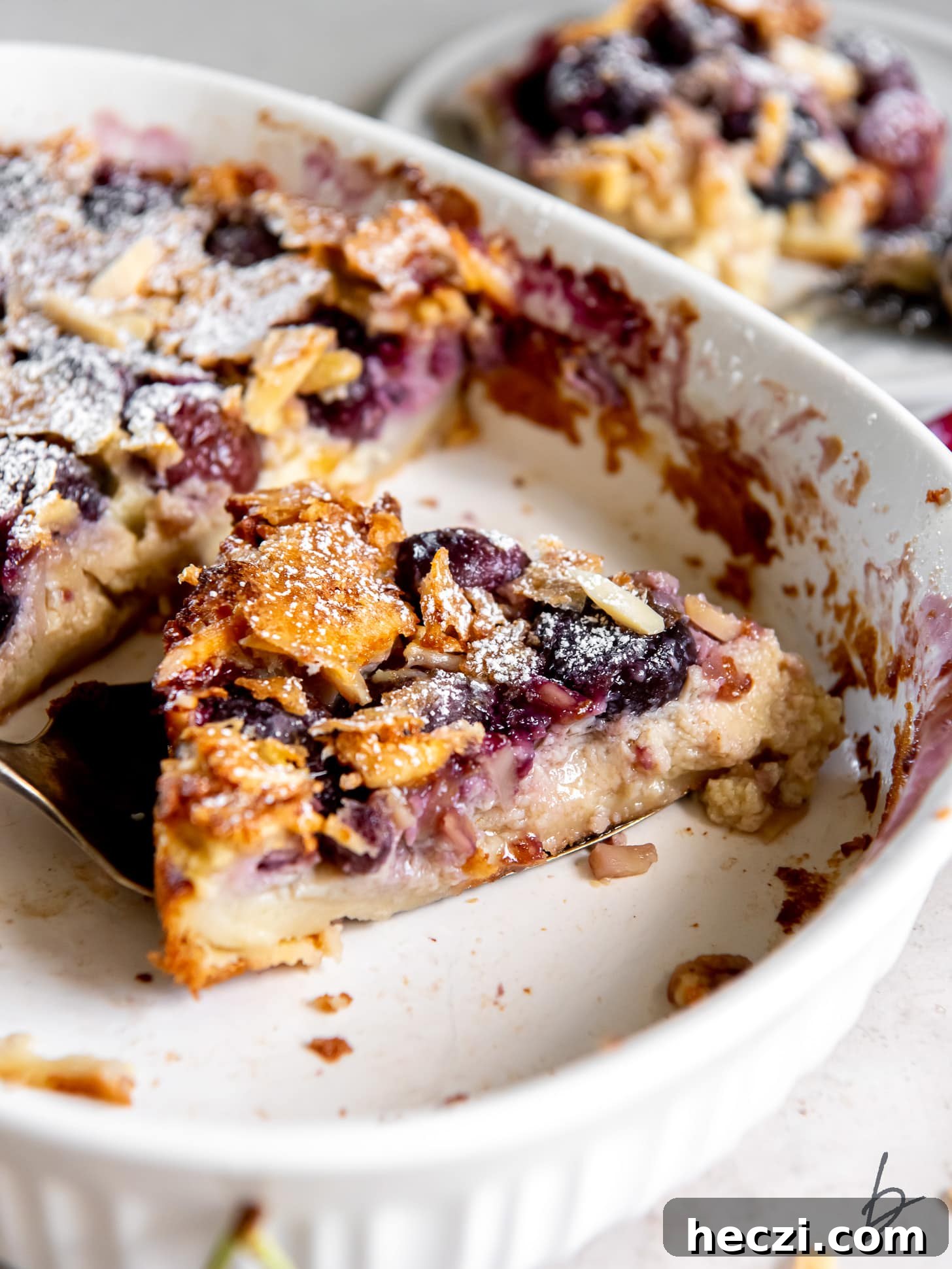slice of cherry clafoutis with almonds in a baking dish.