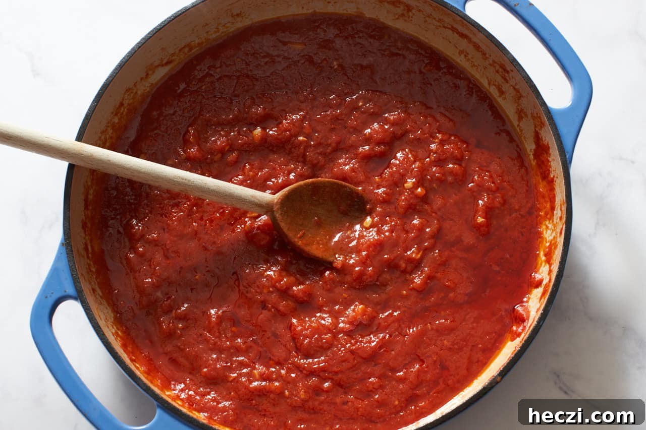 A wooden spoon in a blue casserole pan with tomato sauce.