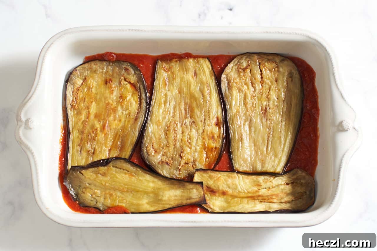 Roasted eggplant slices layered over tomato sauce in a casserole dish.