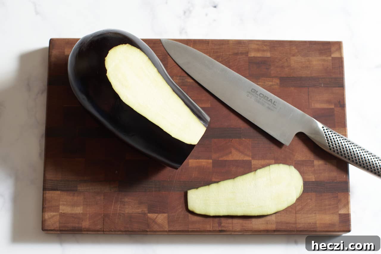 An eggplant on a cutting board with a knife next to it. A small slice of the skin has been cut off.