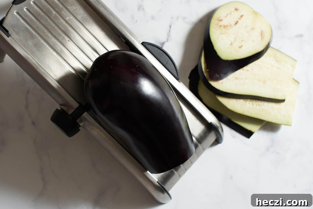 An eggplant being sliced on a mandoline with a few slices of eggplant to the right.