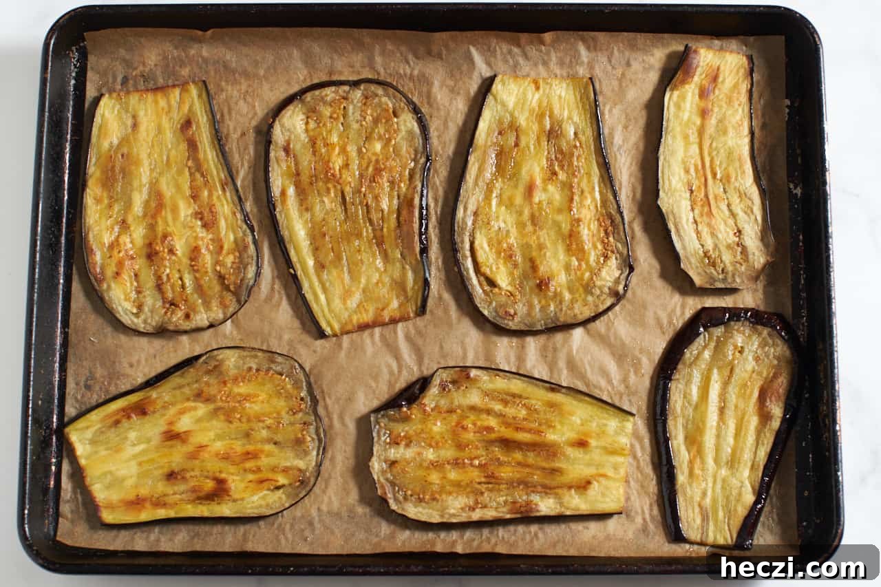 Roasted eggplant slices on parchment paper on a sheet pan.