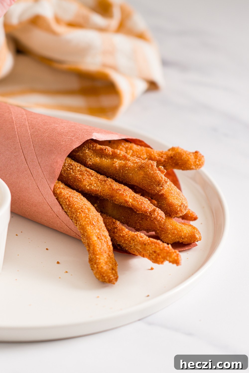 A white plate with fried homemade chicken fries wrapped in contact paper. The plate is on a marble counter with a yellow checkered napkin.